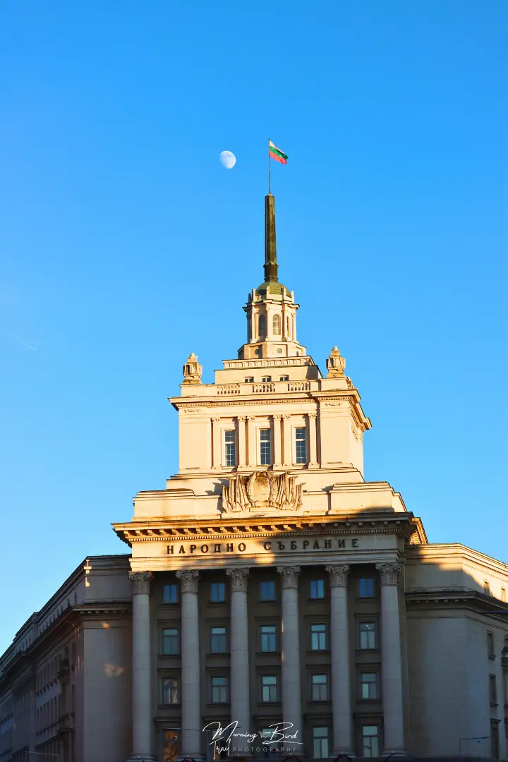 soviet looking building with a Bulgarian flag on the top with a moon in the background in Sofia city centre, Bulgaria