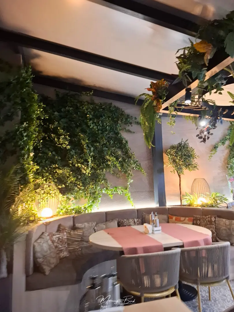 Restaurant in Veliko Tarnovo (Restaurant Asenevtsi) with plastic plants decorating the roof and walls and a half circular sofa with a table and chairs in front 