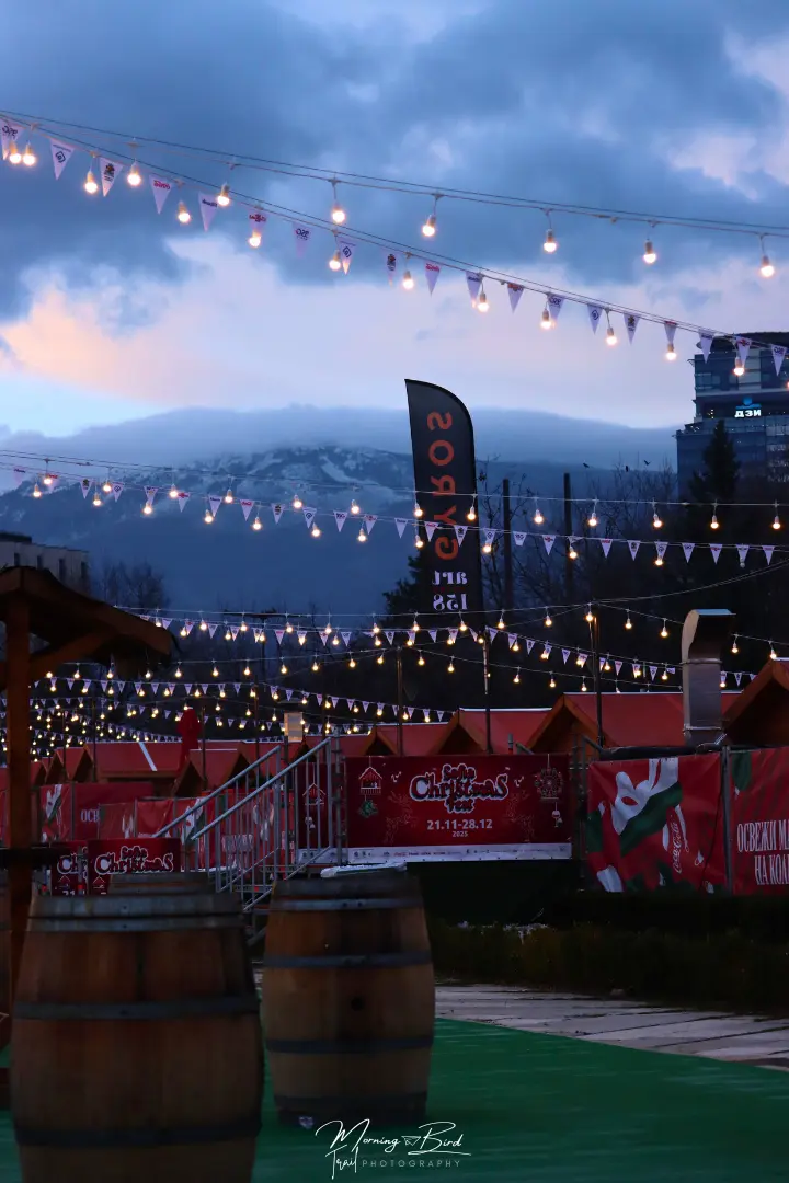 Vitosha mountain with a little bit of snow at the top behind fairy lights above a Christmas market in Sofia, near National Palace of Culture (NDK)