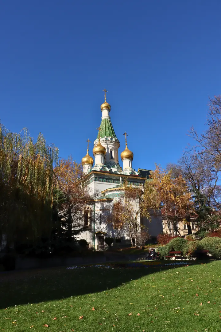 Russian Church of St. Nicholas of Sofia with green and golden roofs, a blue sky and green grass in front, Bulgaria
