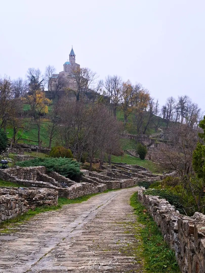Inside the Tsarevets Fortress in Veliko Tarnovo, Bulgaria, with a cobblestone path and ruins of previous houses. On top there is a building of a church