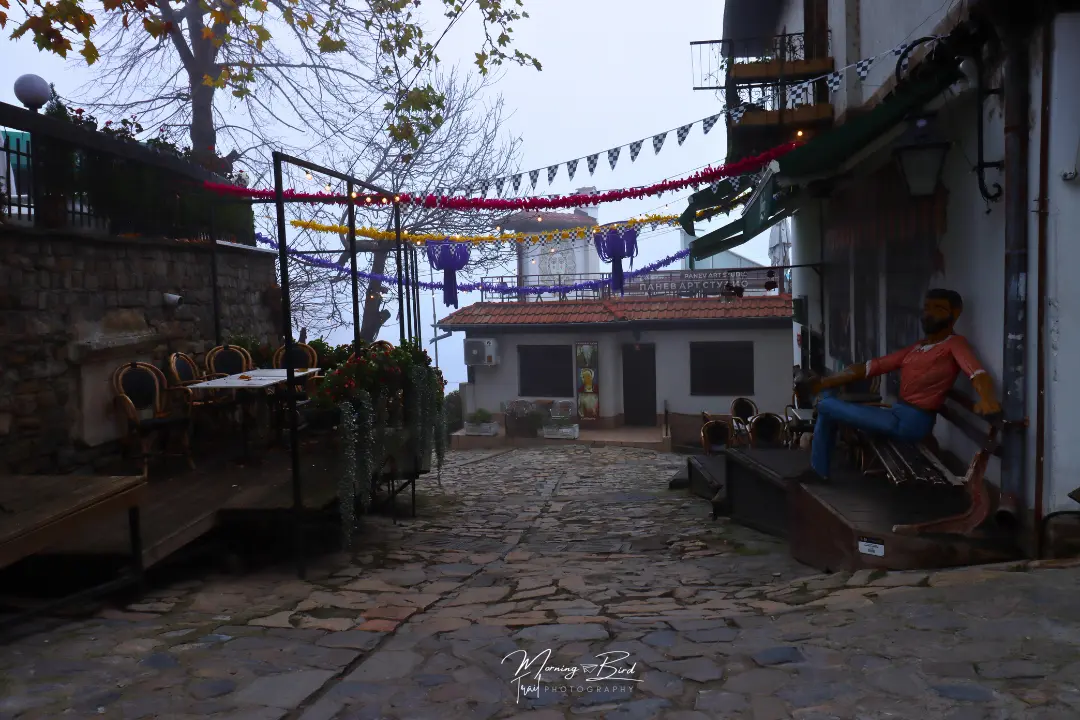 Cobblestone streets with traditional bulgarian houses in Veliko Tarnovo, Bulgaria, decorated with christmas lights. There's also a puppet man sitting on a street bench